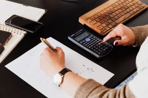 Pessoa usando calculadora enquanto escreve numa folha de papel com caneta, simbolizando regras e cálculo da aposentadoria do servidor público