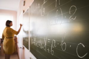 Professora escrevendo cálculos matemáticos com giz na lousa, simbolizando aposentadoria (professor) e mudanças com a Reforma da previdência