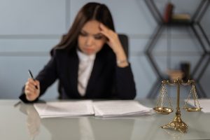 Uma balança sobre a mesa, representando Direito. E uma advogada analisando documentos que estão sobre a mesa, reflexiva. Simbolizando a relação entre tipos de câncer e o direito à aposentadoria