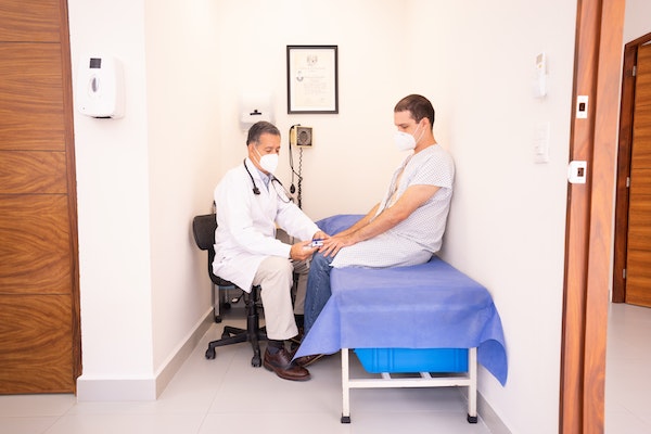 Paciente com sentado sobre uma maca, sendo atendido e examinado por um médico, simbolizando uma consulta de um paciente com câncer e com um oncologista