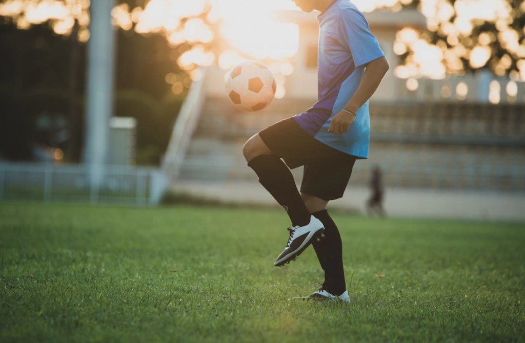 Jogador de futebol em campo fazendo embaixadinha, com a bola de futebol no ar, sobre seu joelho. Representando aposentadoria no esporte para jogadores de futebol