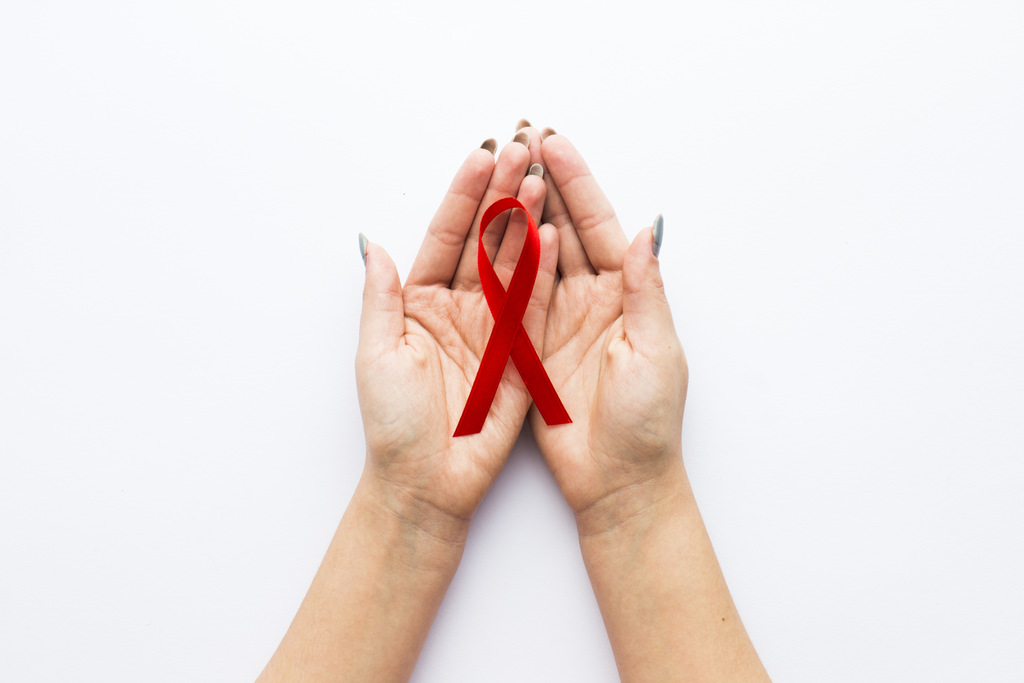 Duas mãos segurando um laço vermelho, símbolo da luta contra AIDS, representando aposentadoria para pessoas com AIDS