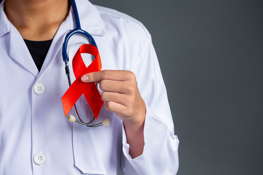 Profissional da saúde com estetoscópio pendurado no pescoço e segurando um laço vermelho, que é símbolo da luta contra AIDS. Simbolizando aposentadoria para soropositivo