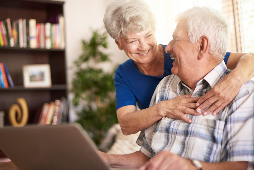 Casal de idosos abraçados, sorrindo se entreolhando com notebook a frente deles, simbolizando as vantagens das principais aposentadorias do INSS