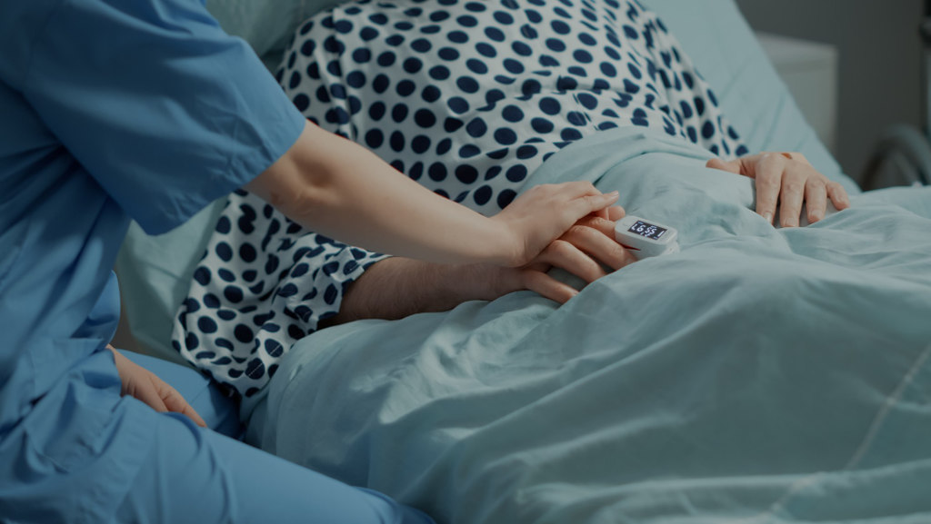 Pessoa com roupa de hospital dando a mão para um paciente no leito, simbolizando doenças que dão direito a aposentadoria por invalidez