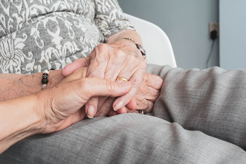 Simbolizando revisão da vida toda: Mão feminina de idosa com aliança segurando outra mão também enrugada
