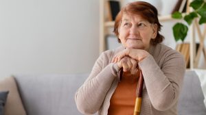 Senhora apoiada com o rosto sobre mãos que estão em uma bengala, representando revisão de atividades concomitantes