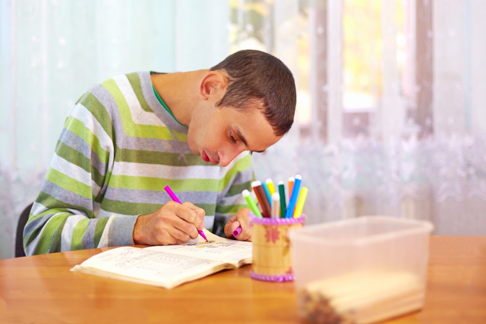 Pessoa escrevendo em um caderno com canetas coloridas em uma mesa