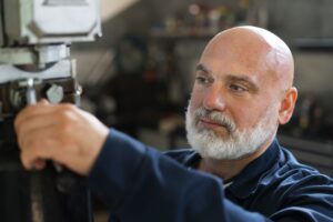 Trabalhador mecânico de barba branca operando maquinário industrial, representando segurados que possuem direito à aposentadoria especial por insalubridade em 2026.